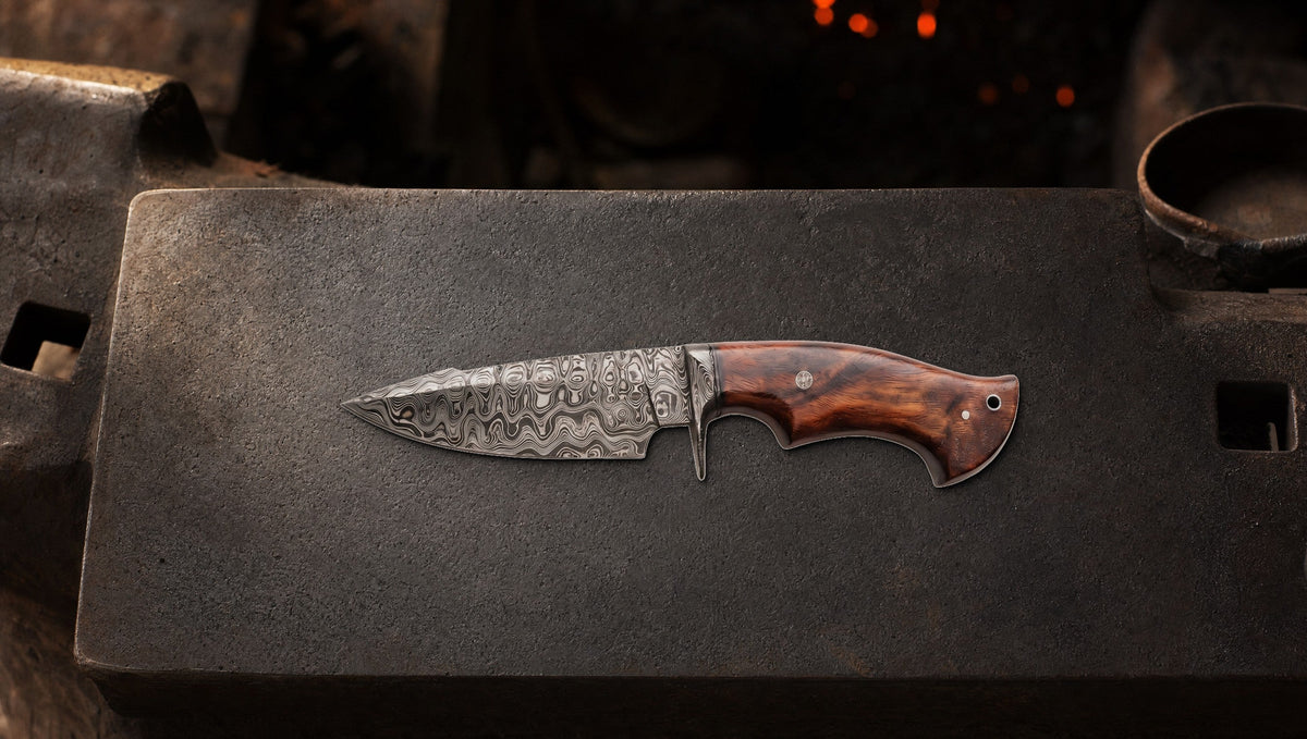 Predator Hunter Damascus knife with a walnut handle on an anvil, the layered pattern lit from the side