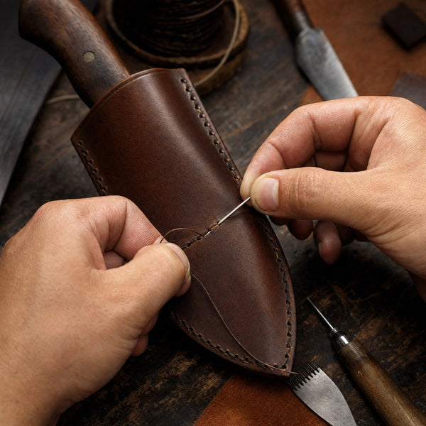 Hands stitching a leather sheath on the bench