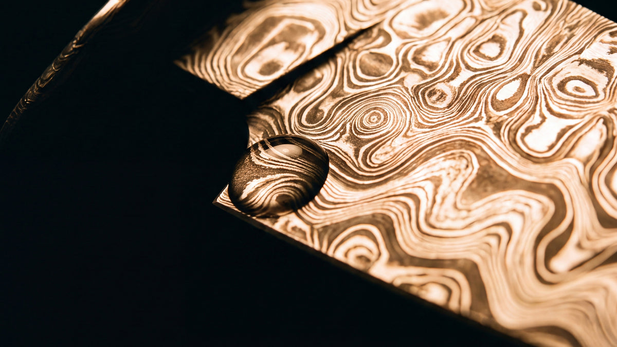 Warm light across the swirled pattern of a Damascus billet